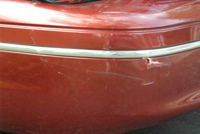 Red car bumper with chrome trim, showing scratches and a dent