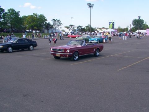 1998 Ford Taurus - A classic red Ford Mustang convertible is parked in a lot during a car meet.