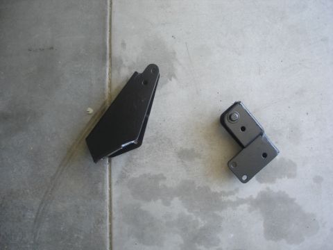 1987 Ford Bronco - Two black metal brackets are shown on a concrete surface. One bracket is a single piece with a triangular shape and two holes. The other br…