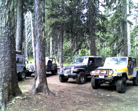 2005 Jeep Wrangler - Four lifted Jeeps, a yellow Wrangler with doors off, a black soft-top Wrangler, a topless dark Jeep and a silver rig with roof rack, parked…