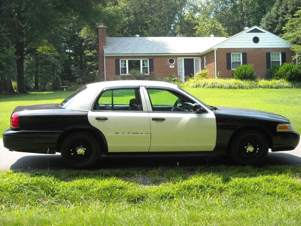 Black and white Ford Crown Victoria sedan parked in front of a house.