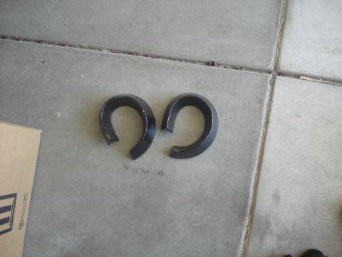 1987 Ford Bronco - Two black metal horseshoe-shaped spacers are shown on a concrete surface. A cardboard box is partially visible on the left side of the imag…