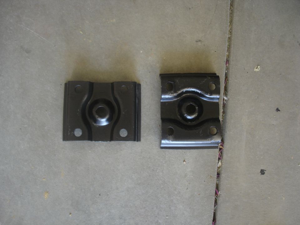 Two black metal brackets with central circular indentations and mounting holes.