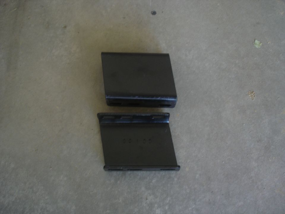Two black metal brackets on a concrete surface. The bottom bracket has "40100" stamped on it.