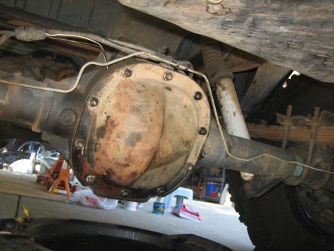 1995 Ford Bronco - The underside of a vehicle shows a differential housing with a rusty cover and bolts. Brake lines and a shock absorber are also visible, al…
