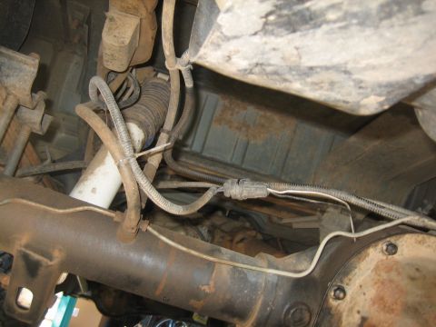 1995 Ford Bronco - The underside of a vehicle, showing the rear differential, suspension components, and fuel tank. Various lines and electrical connectors ar…