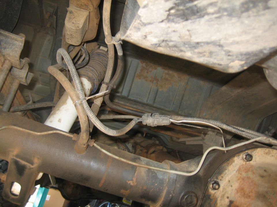 Underside of a vehicle showing rear differential, suspension, and fuel tank with rust.