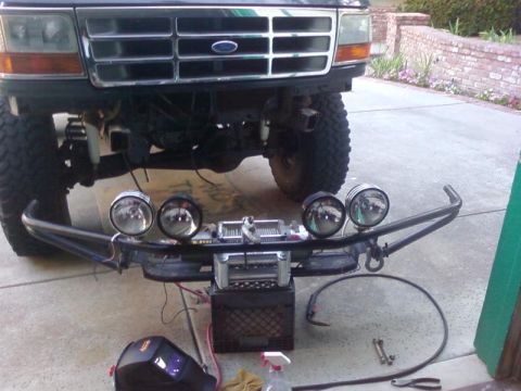 1995 Ford Bronco - A modified front bumper with a winch and multiple spotlights is mounted to the front of a dark-colored Ford Bronco. The vehicle is lifted w…