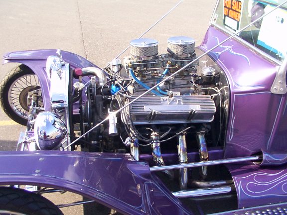 Purple hot rod with exposed V8 engine, dual carburetors, and chrome headers