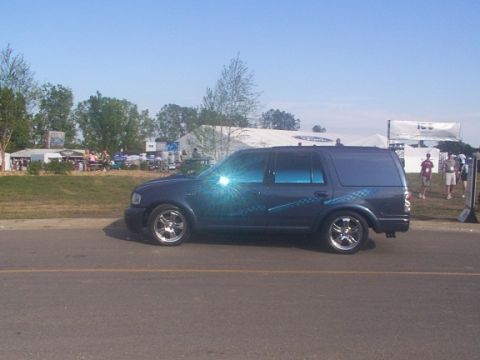 1998 Ford Taurus - A dark blue SUV is parked on the side of a road with tents and people in the background.