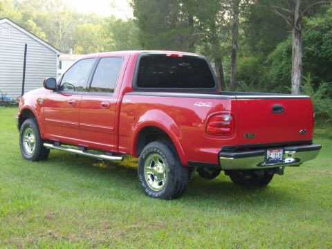 2007 Ford Mustang - Photograph of a red Ford F-150 crew-cab pickup parked on a lawn, rear three-quarter angle.