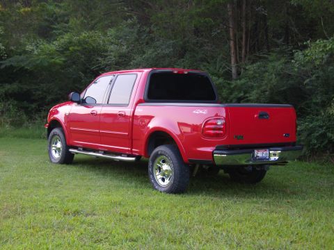 2007 Ford Mustang - Photograph of a red Ford F-150 crew-cab pickup on grass in front of a tree line.