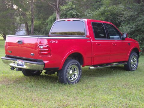 2007 Ford Mustang - Photograph of a red Ford F-150 crew-cab pickup parked on grass near trees.