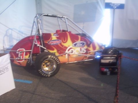 1998 Ford Taurus - A race car with a flame paint scheme and Ford Focus branding is displayed indoors.