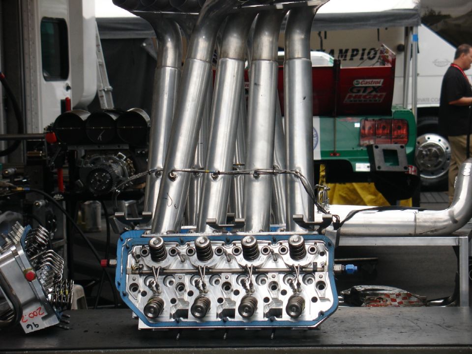 Close-up of a V8 engine's exhaust headers and valve train with polished metal pipes.