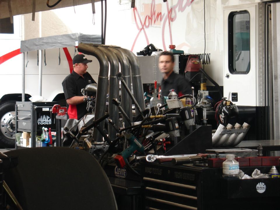 Mechanics working on a large engine with multiple exhaust pipes in a garage.