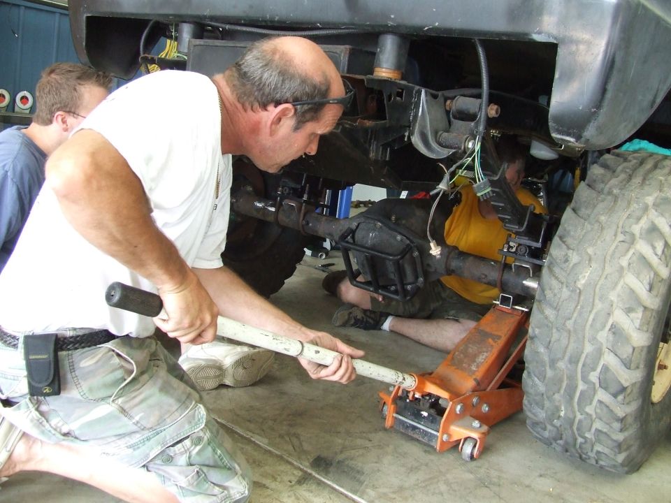 Men working on vehicle rear axle and suspension with a jack