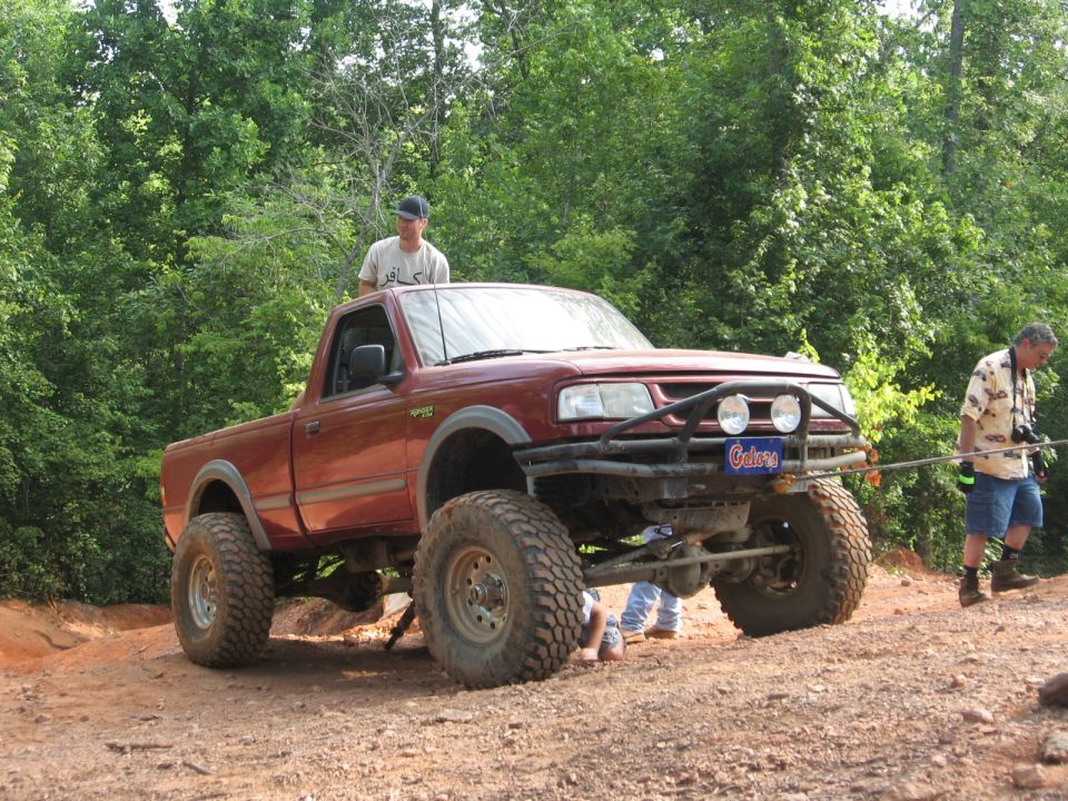 Lifted red pickup truck on a dirt trail with a man in the bed.