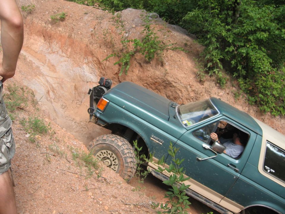 Green and tan Ford Bronco off-roading on a steep sandy hill.