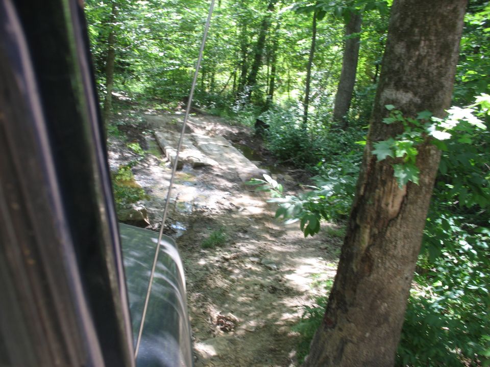 View past a vehicle of a rocky descending trail through green woods