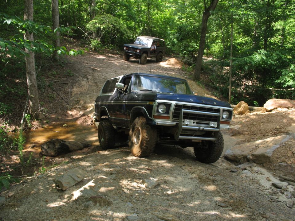 Blue Ford Bronco crawling rocks on a wooded trail with second truck behind
