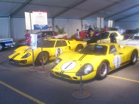 1998 Ford Taurus - Two vintage Ford GT40 race cars are parked under a tent, one with racing number 1 and the other with number 8.
