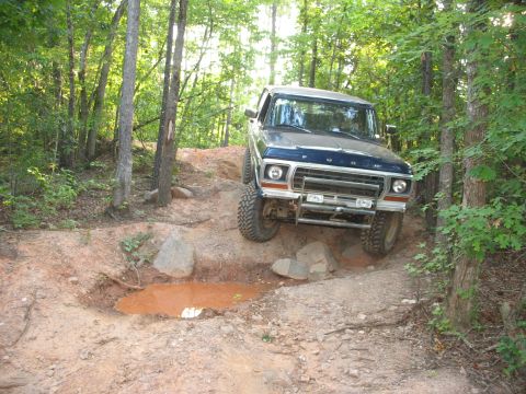 1978 Ford Bronco - A blue 1978 Ford Bronco navigates a rocky, wooded off-road trail.