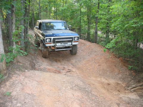 1978 Ford Bronco - A blue 1978 Ford Bronco navigates a dirt trail through a wooded area.