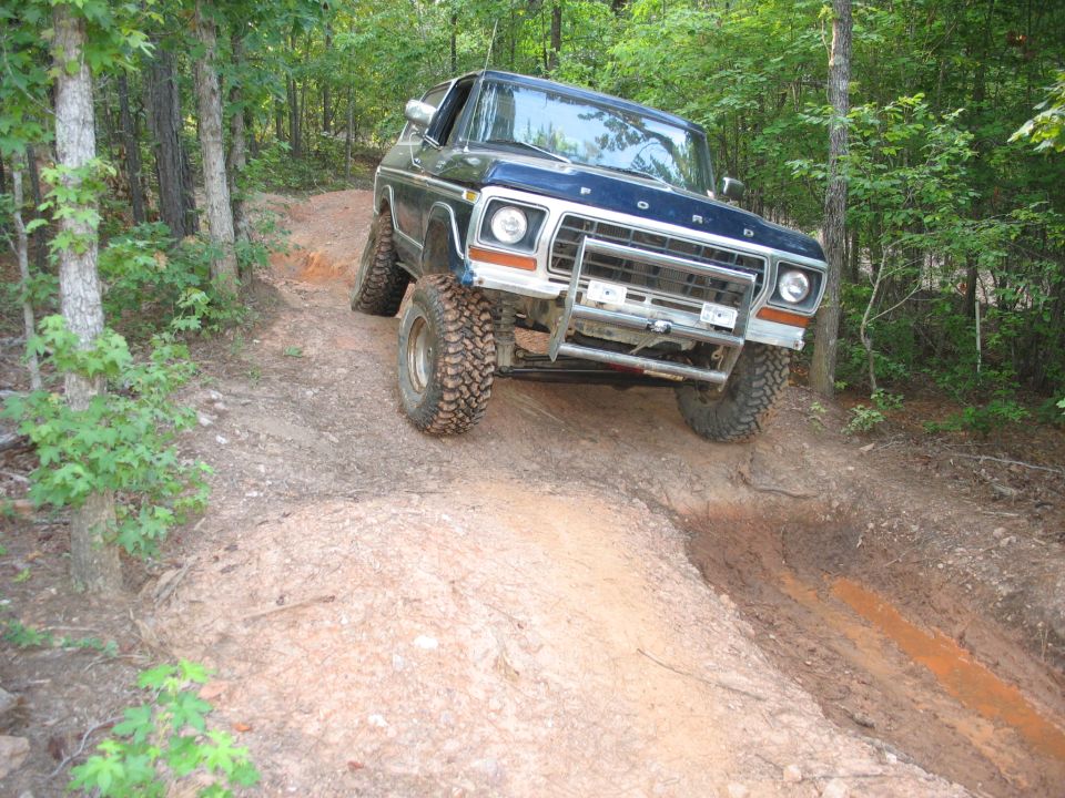 1978 Ford Bronco climbing a steep dirt trail with trees on either side