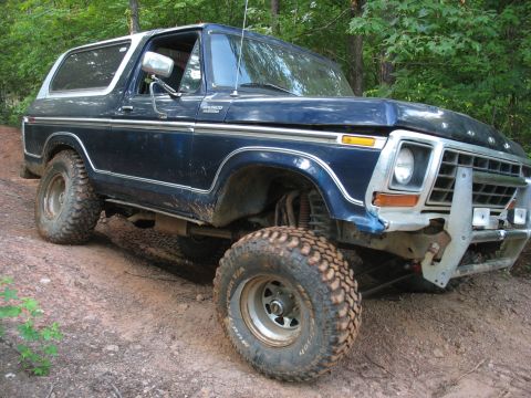 1978 Ford Bronco - A blue 1978 Ford Bronco with a white hardtop navigates a muddy off-road path.