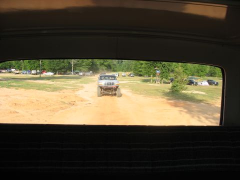 1978 Ford Bronco - A silver pickup truck with oversized tires navigates a dirt track, with other vehicles and tents visible in the background.