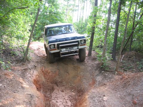 1978 Ford Bronco - A 1978 Ford Bronco navigates a steep, muddy trail surrounded by trees.