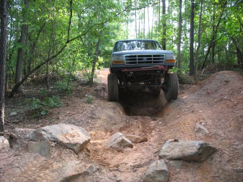 1978 Ford Bronco - A lifted truck tackles a challenging off-road course through a wooded area.