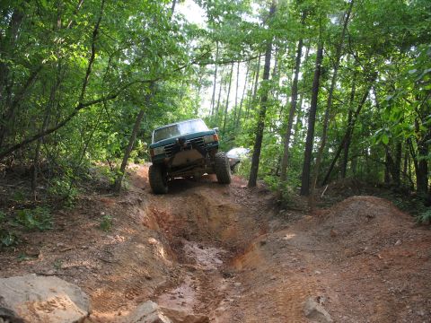 1978 Ford Bronco - An off-road vehicle navigates a challenging muddy trail through a wooded area.