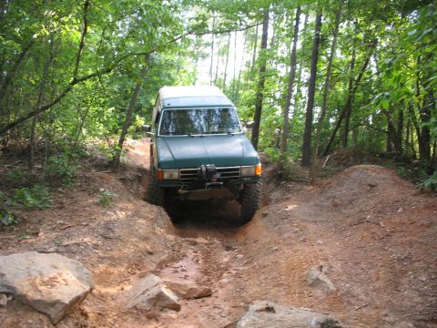1978 Ford Bronco - A green SUV navigates a challenging dirt path surrounded by dense trees.