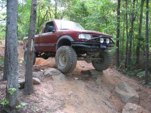 1978 Ford Bronco - A red pickup truck navigates a challenging off-road trail with large tires and a modified bumper.