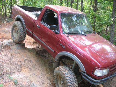 1978 Ford Bronco - This red pickup truck is shown off-roading on a dirt path with large tires and modified suspension.