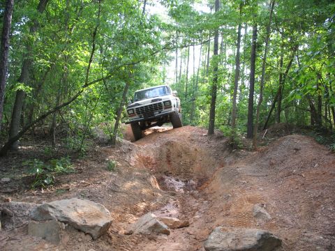 1978 Ford Bronco - 1978 Ford Bronco navigating a challenging off-road trail through a forest.