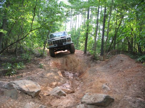 1978 Ford Bronco - A 1978 Ford Bronco navigates a challenging off-road trail through a wooded area.