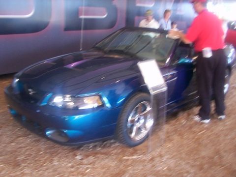 1998 Ford Taurus - A person cleans the windshield of a blue convertible sports car on display.