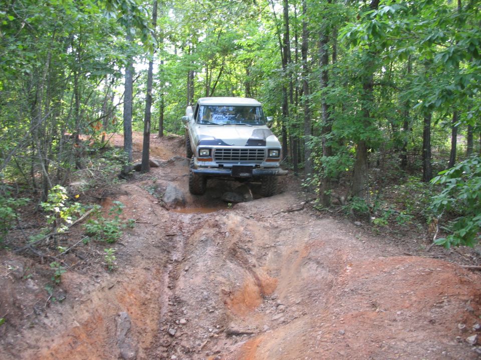 Ford F-Series truck driving on a muddy, wooded trail