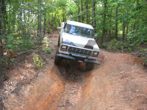 1978 Ford Bronco - A 1978 Ford Bronco navigates a muddy, rutted path through a wooded area.