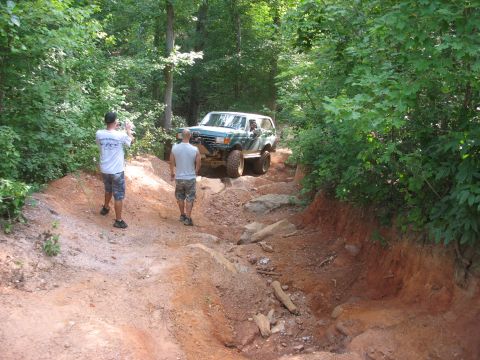 1978 Ford Bronco - A green SUV tackles a challenging off-road course in a wooded area.