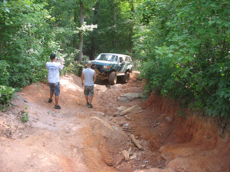 Green SUV navigating a steep, rocky off-road trail with two people watching