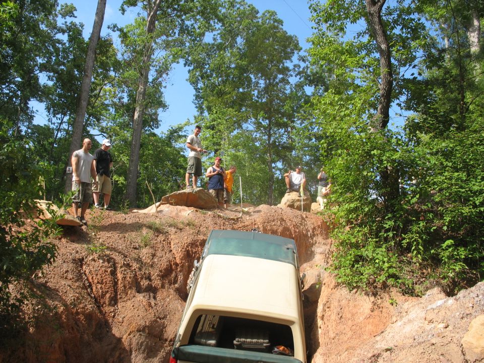 Two-tone green and cream 1978 Ford Bronco descending a steep dirt ravine with onlookers