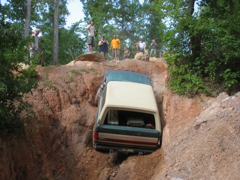 1978 Ford Bronco - A group of people watch as a green and tan SUV navigates a challenging off-road trail.