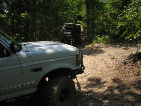 1978 Ford Bronco - Two Broncos are parked on a dirt trail surrounded by trees.
