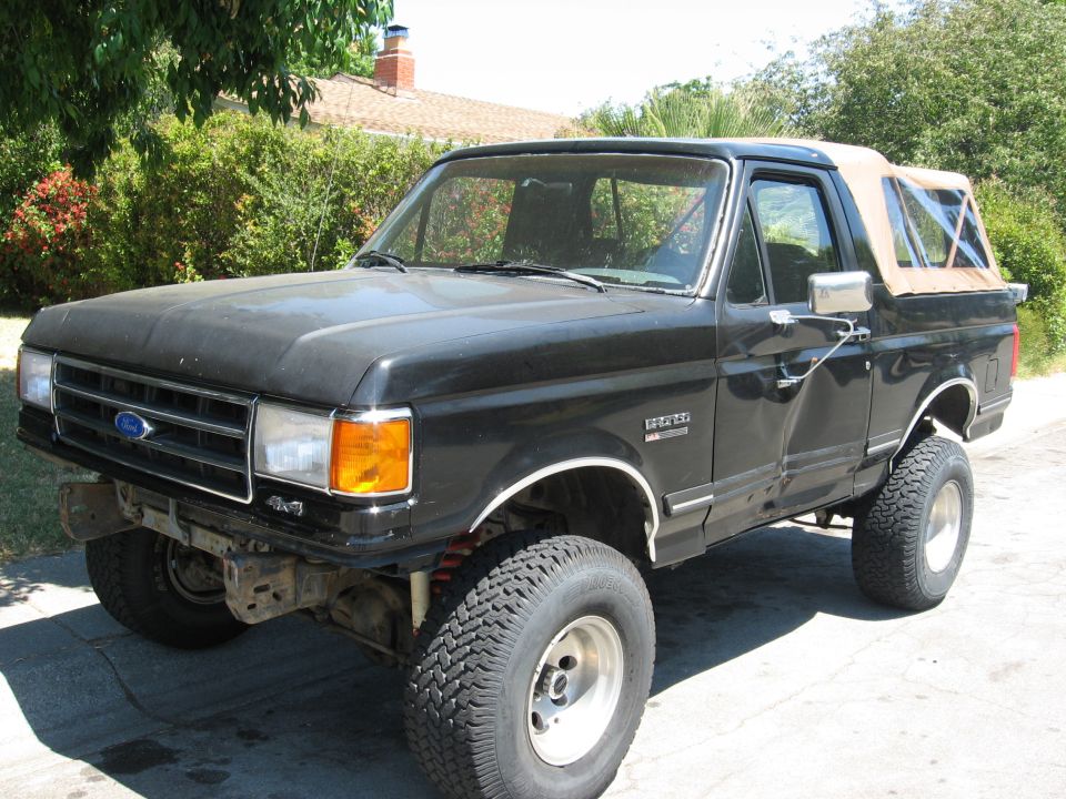 Lifted black Ford Bronco with tan soft top and no front bumper, 3/4 front view