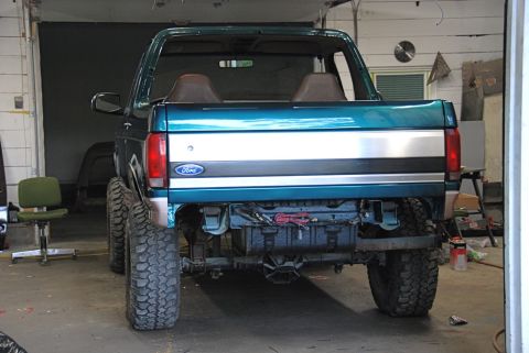1996 Ford Bronco - The rear of a teal Ford Bronco is shown in a garage, with its bumper removed and large off-road tires installed.