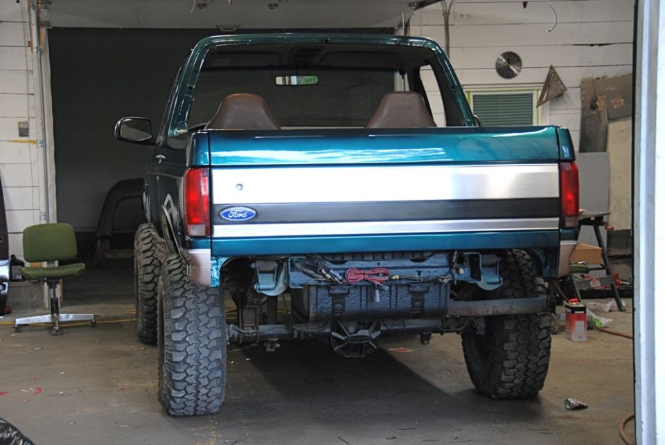Rear view of a teal Ford Bronco with large tires, missing its rear bumper